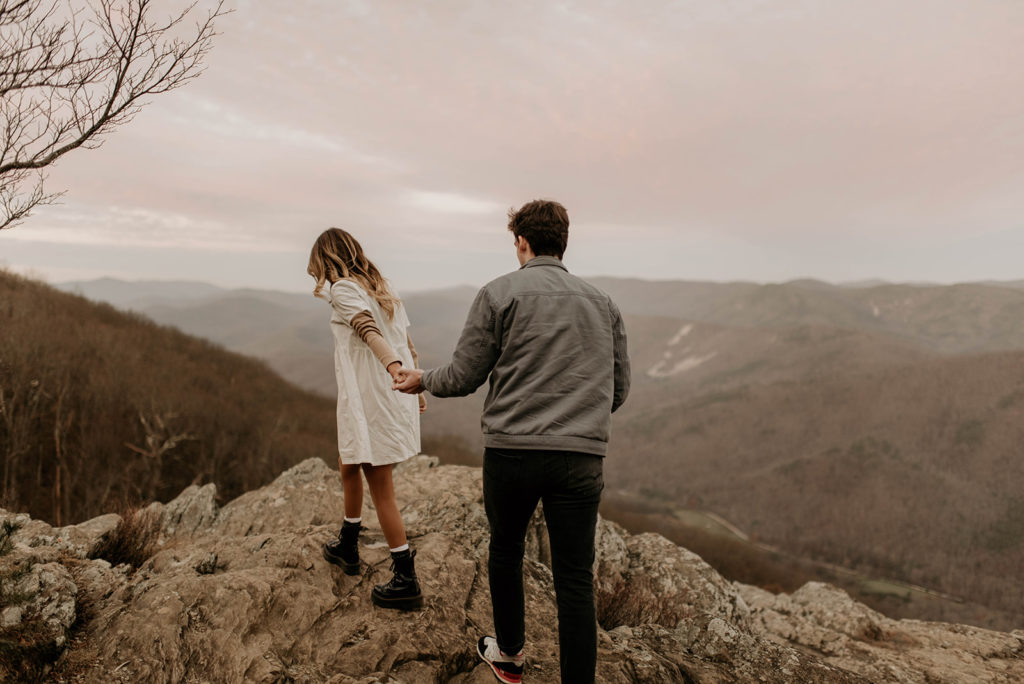 Couple walks holding hands along overlook at surprise proposal 