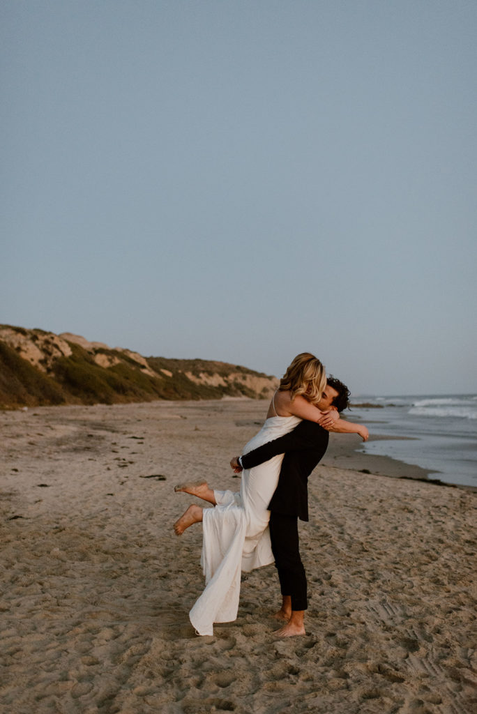 Couple embraces on beach at adventurous elopement