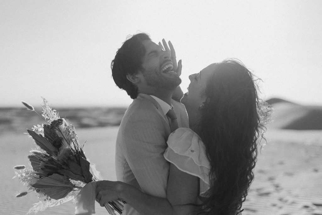 Couple embraces laughing at sand dunes elopement