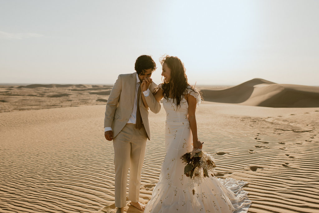 Groom kisses bride's hand at sand dunes elopement