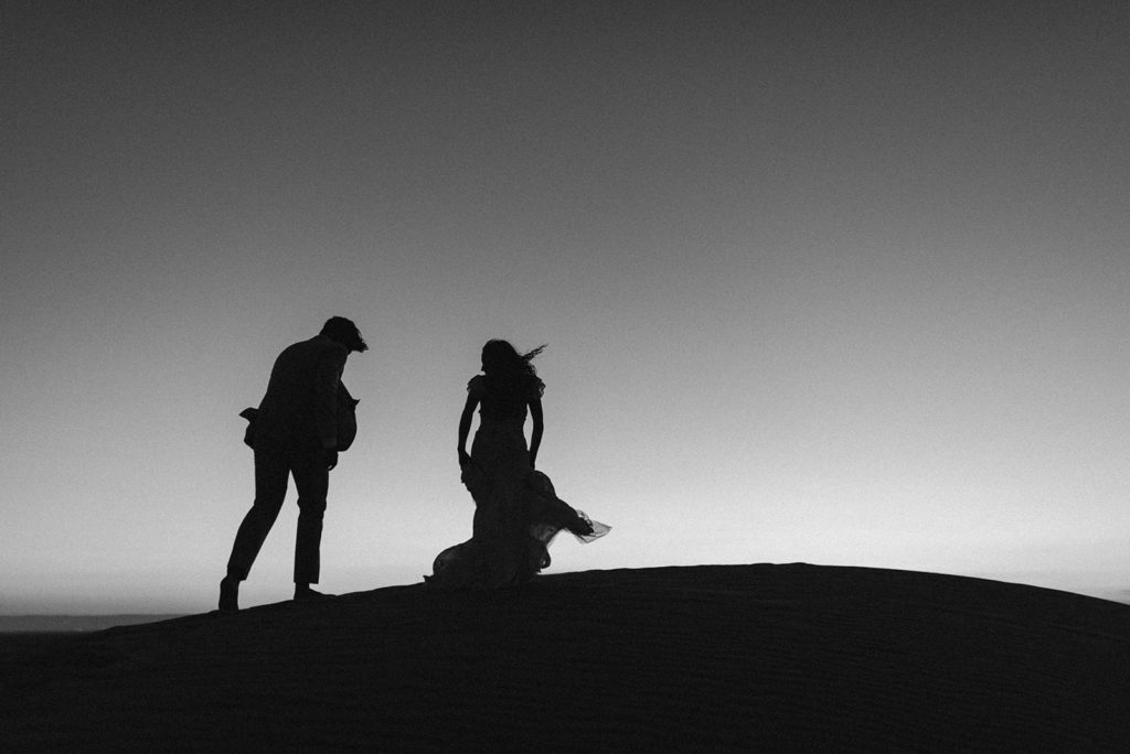 Couple walks over sand dunes at elopement