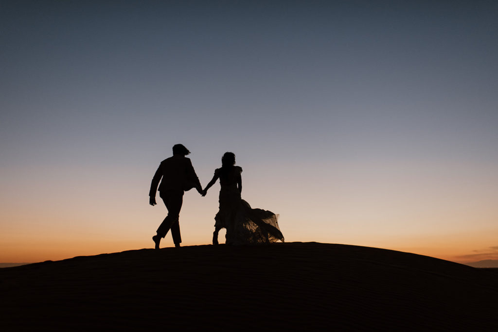 Couple walks holding hands at sand dunes elopement