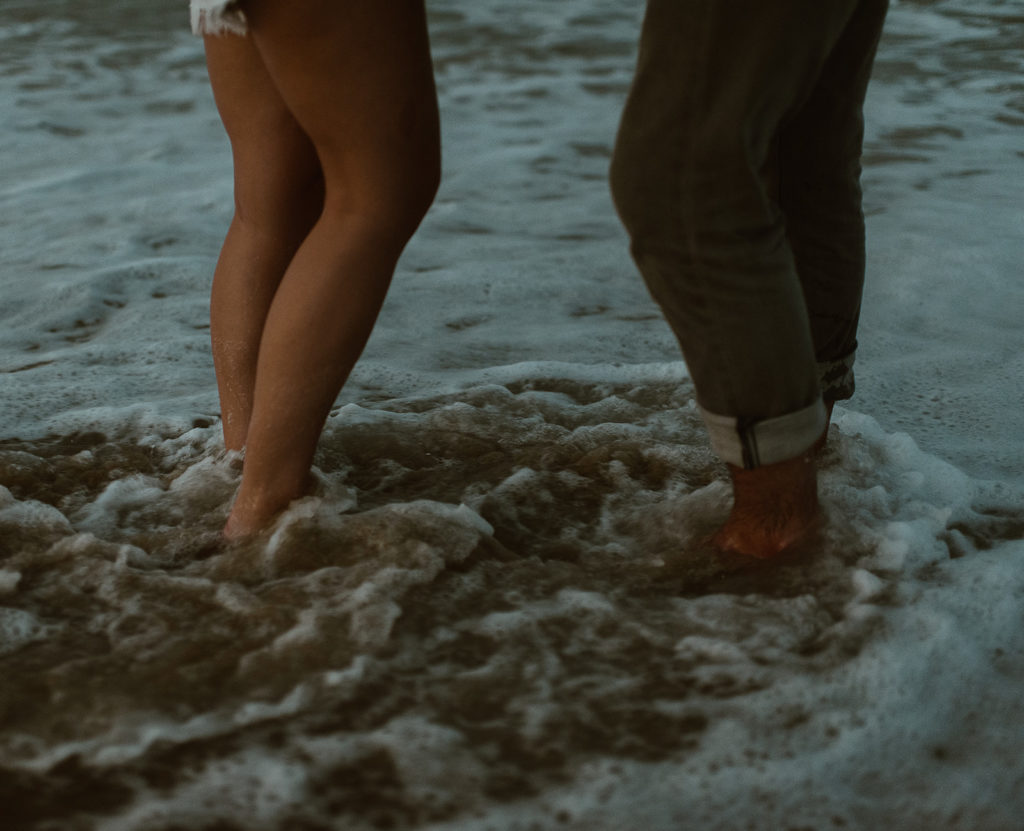 Waves crash over couples' feet at beach adventure session