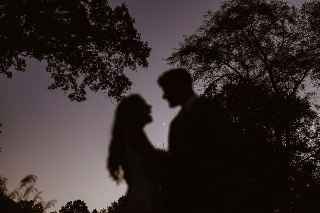 Couple kisses at night under the moon at outdoor wedding 
