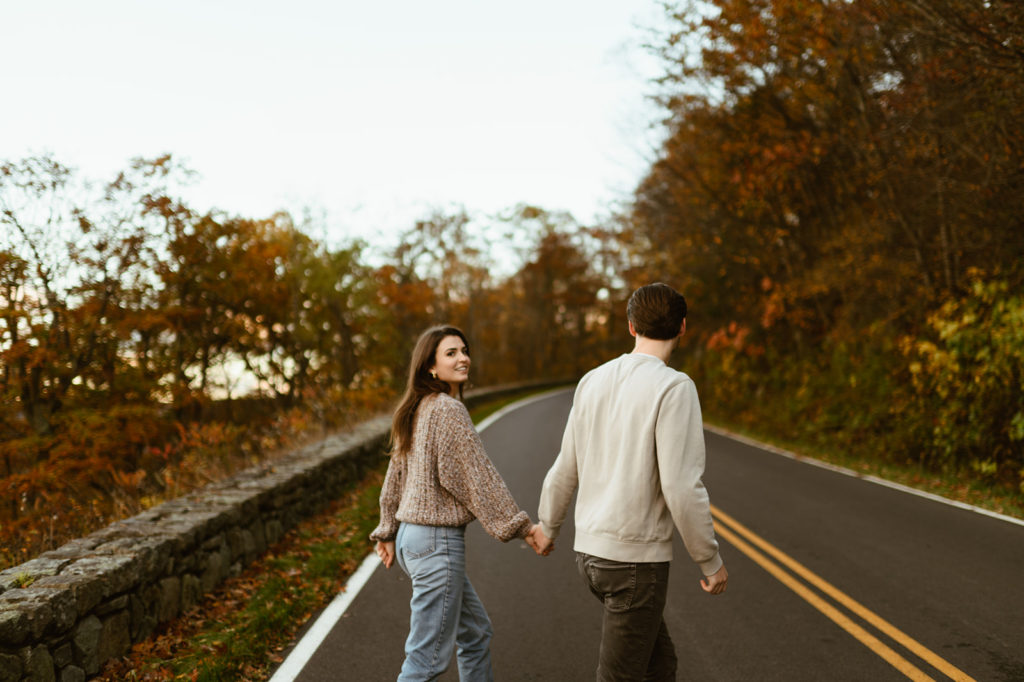 Couple holds hands walking at fall windy engagement session
