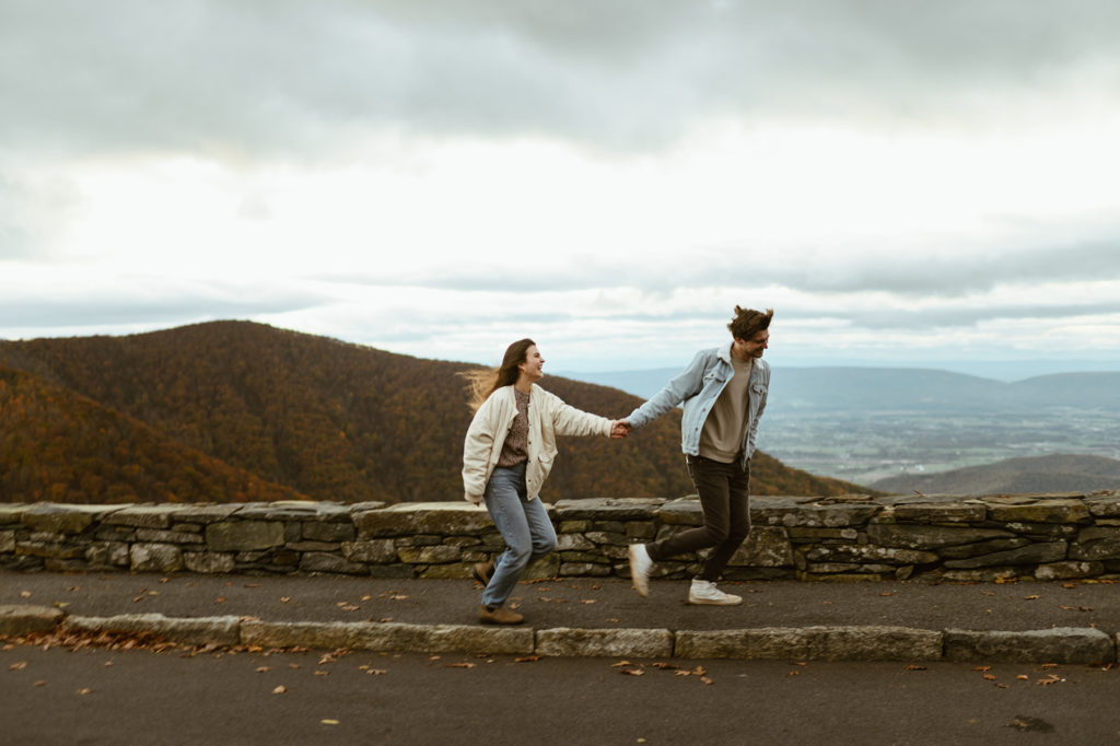 Couple runs holding hands at windy fall engagement session 