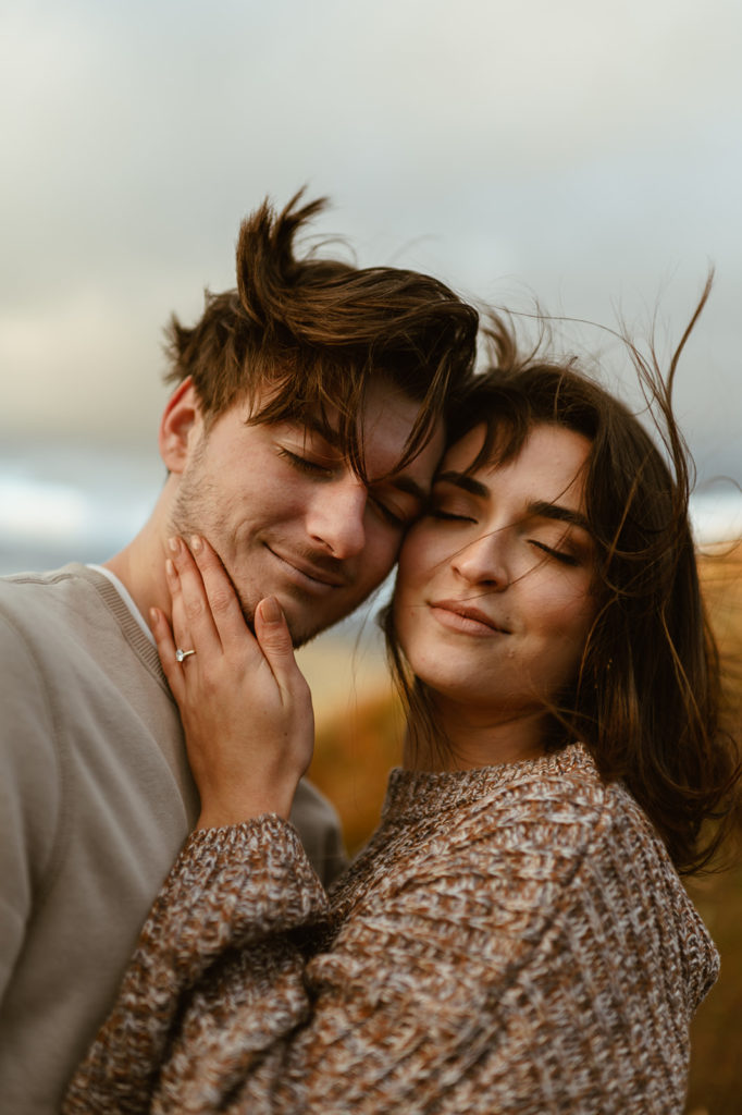 Couple embraces cheek to cheek at fall windy engagement session