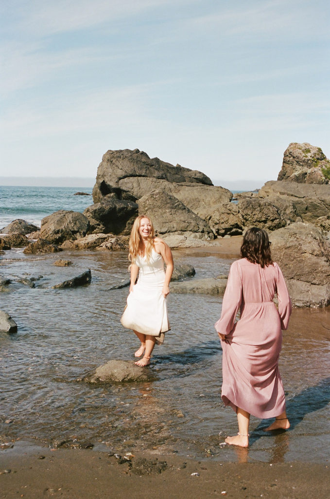Bride walks through water with bridesmaid at beach elopement