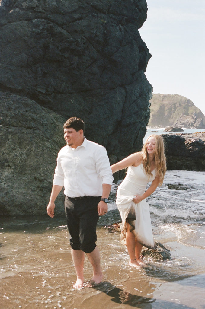Bride and groom walk through water at beach elopement