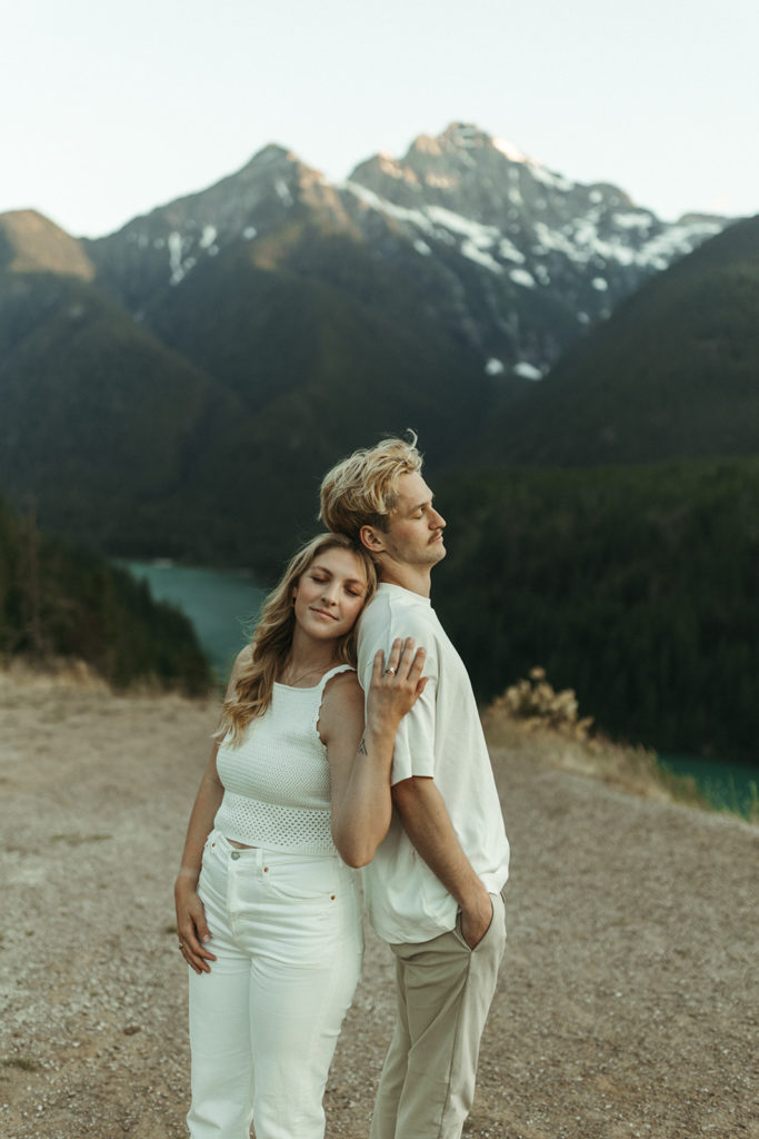 Couple stands back to back at Cascades mountain engagement shoot