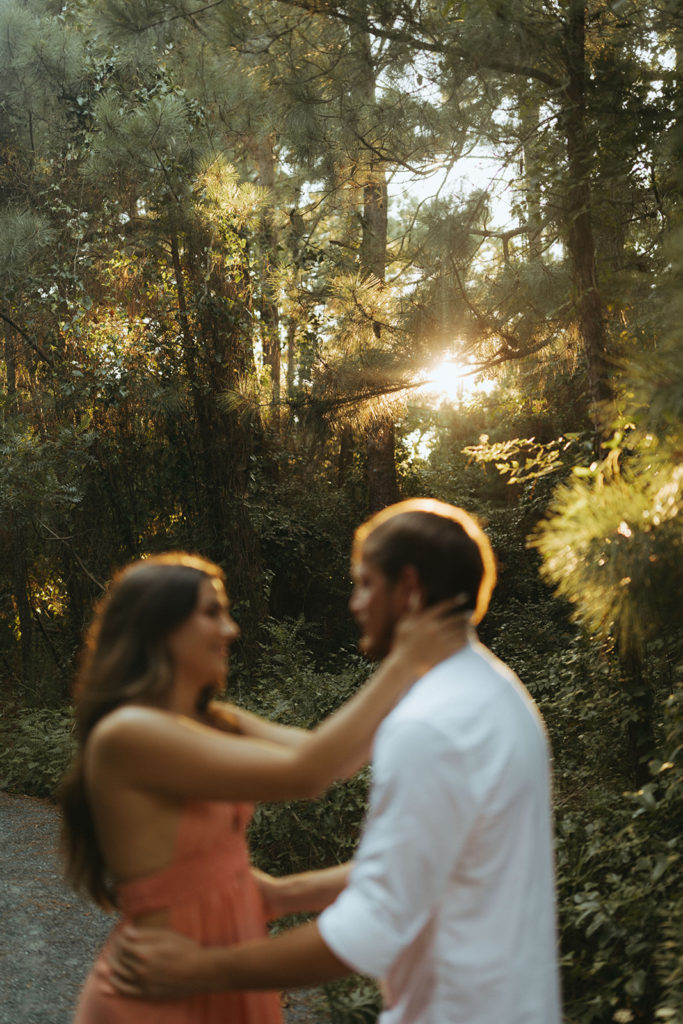 couple prepares to kiss under sunset peeking through trees