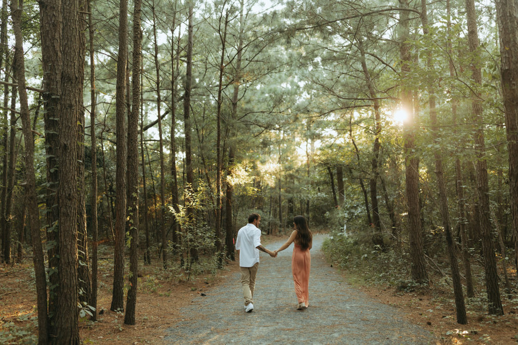 couple walks holding hands through sunset trees captured by Virginia Beach photographer