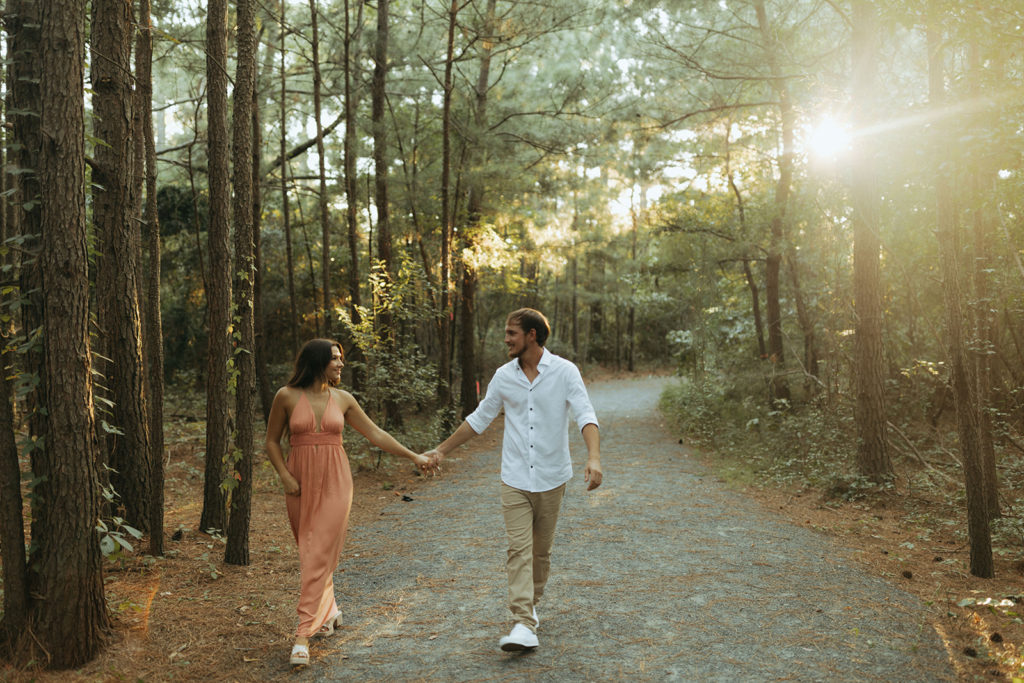couple holds hands through sunset-lit forest
