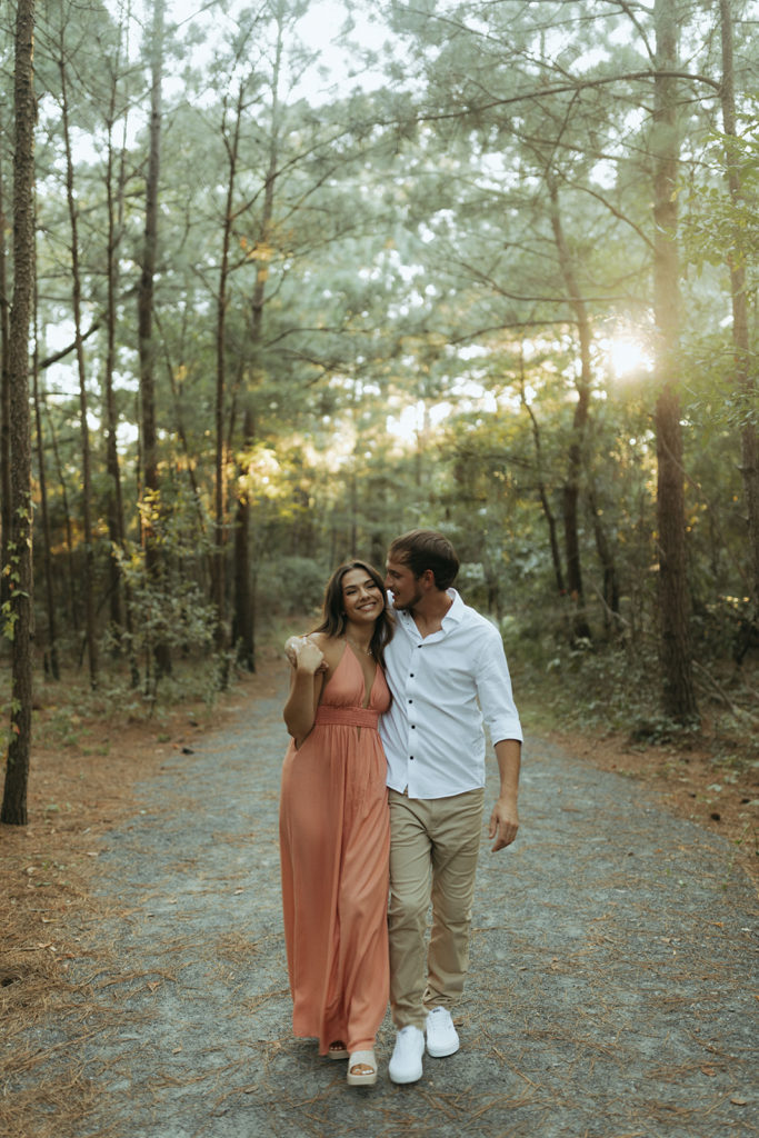 couple holds hands walking through forest at sunset