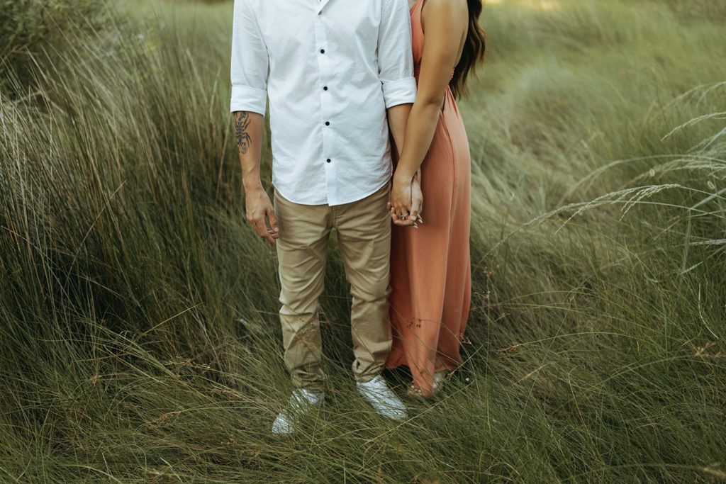 couple holds hands in high green grass at Virginia Beach photographer photoshoot