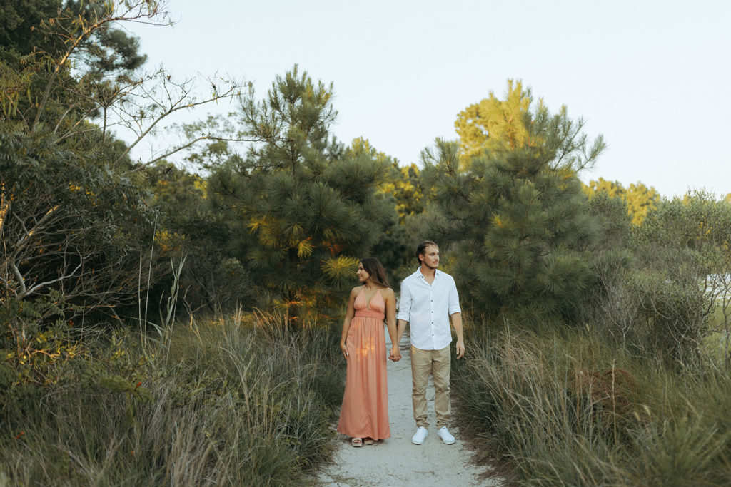 couple holds hands facing other directions at sunset grassy path
