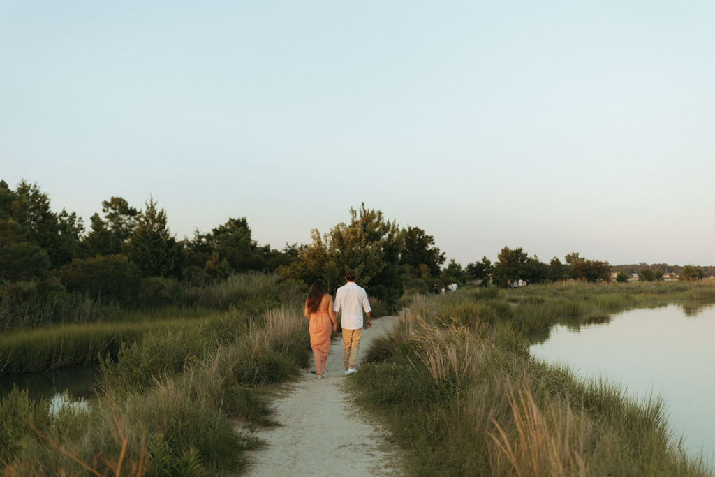 couple walks along grassy waterside at sunset