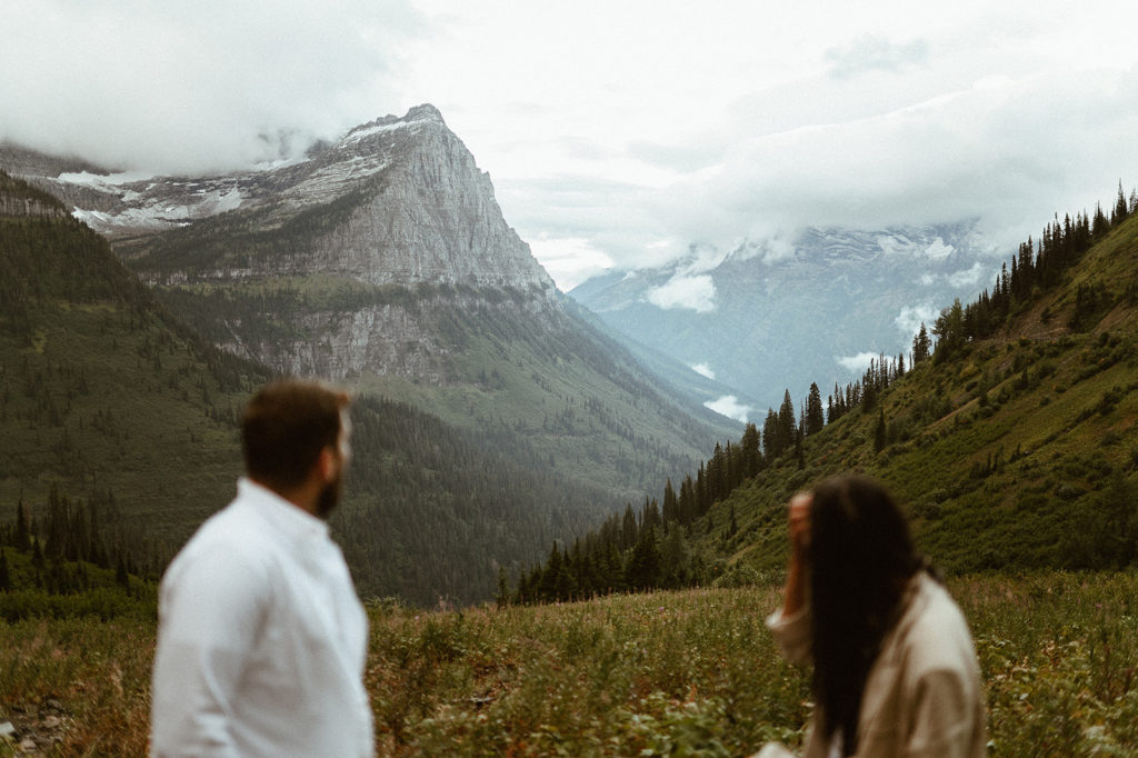 Couple stands in field looking at mountains at Glacier National Park elopement