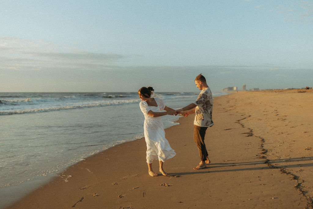 couple holds hands at Virginia Beach sunrise engagement session with travel photographer