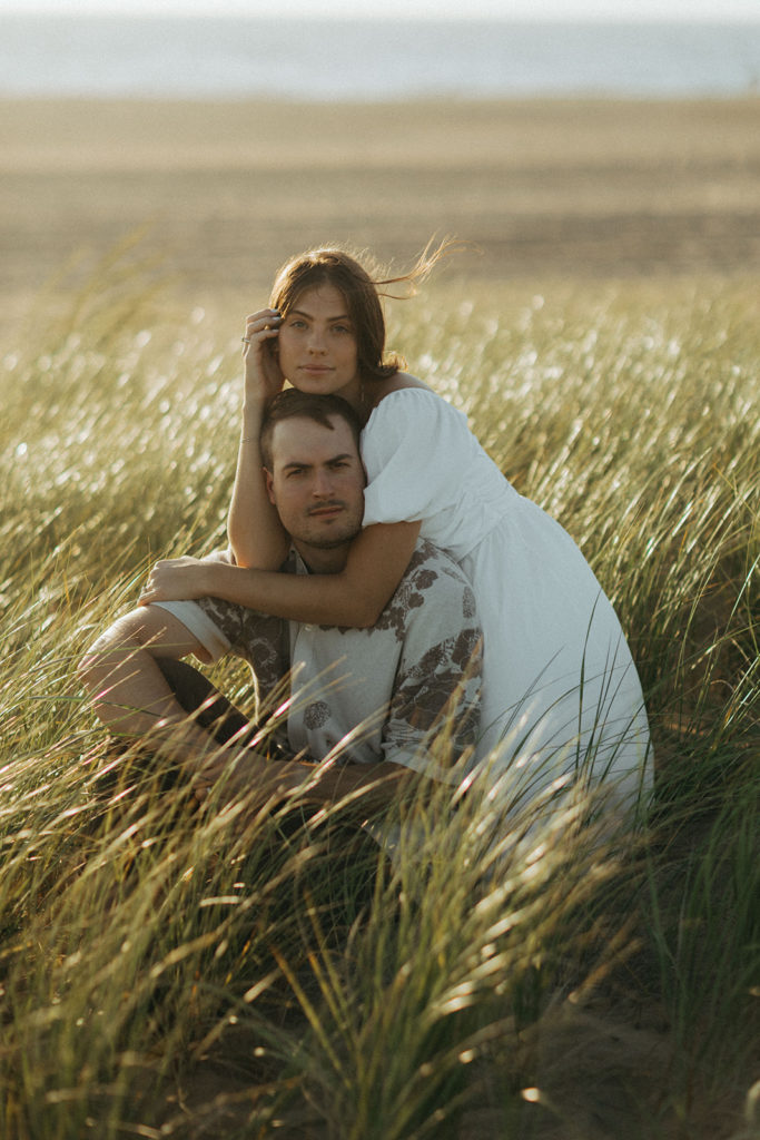 couple embraces in grassy sand dunes at sunrise engagement session