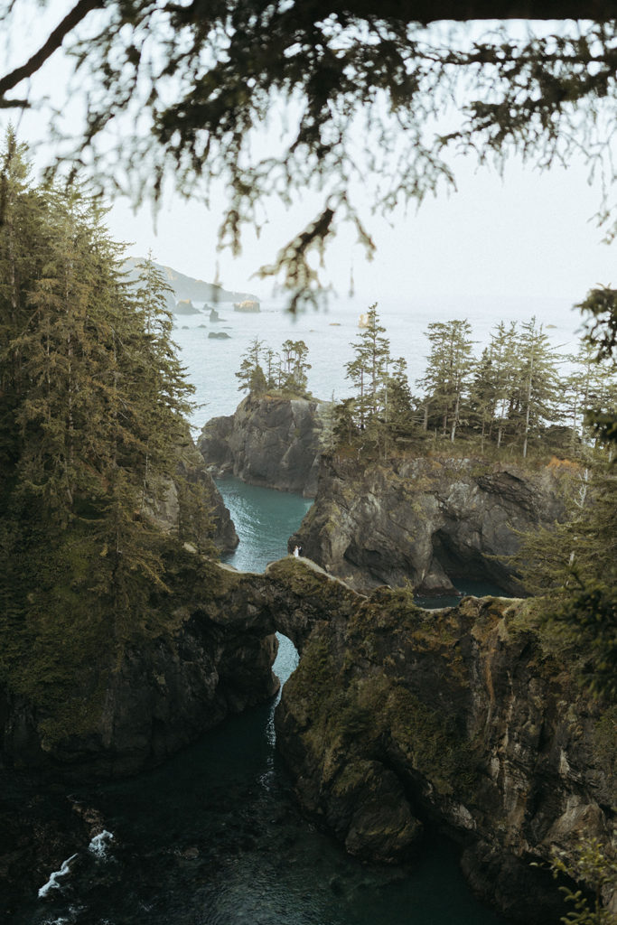 couple stands on overlook at a distance at Oregon Coast elopement wedding photoshoot