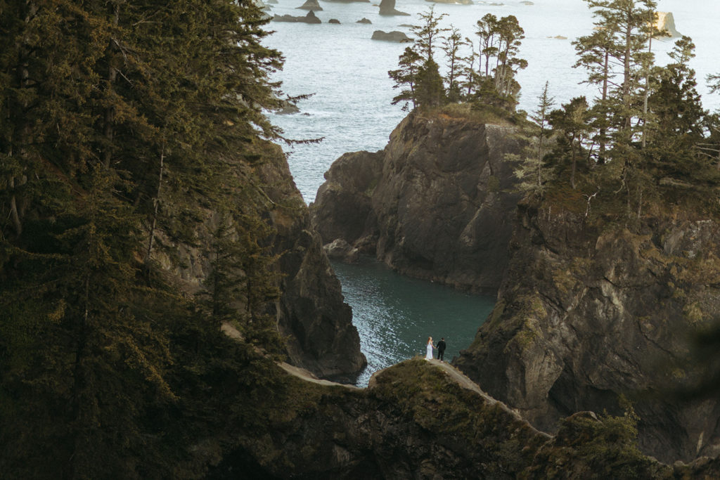 couple stands on overlook at a distance at Oregon Coast elopement wedding photoshoot