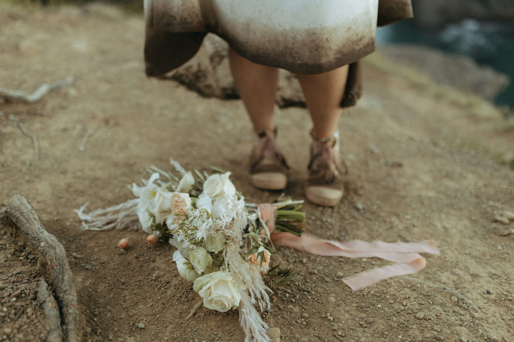 bride trashes the dress beside wedding bouquet at Oregon coast adventure elopement