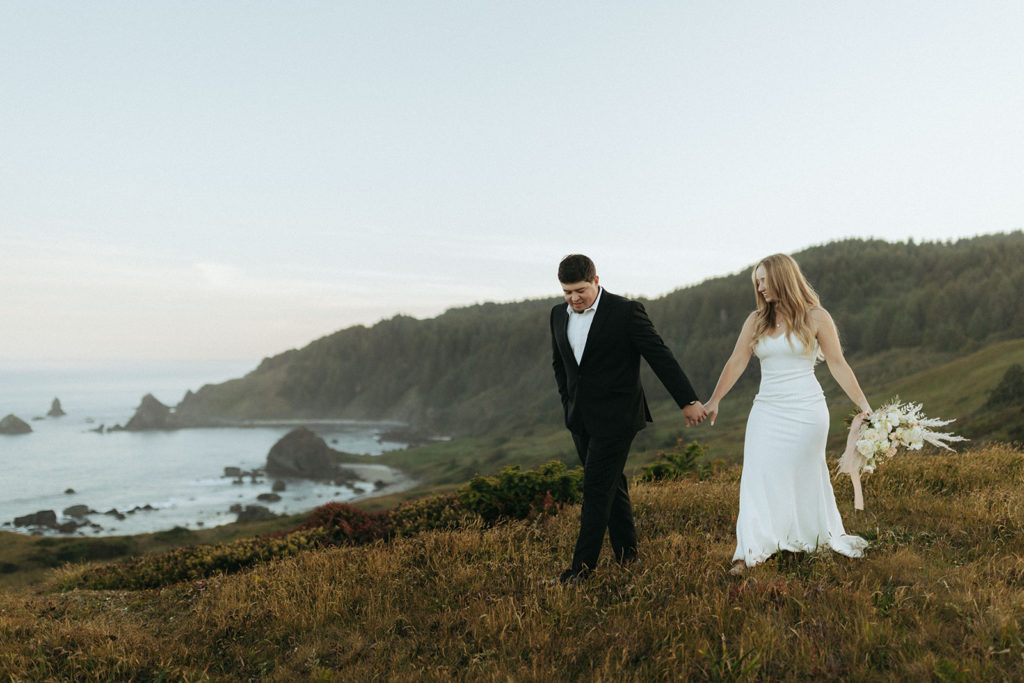 couple walks through field at Oregon Coast elopement wedding photoshoot