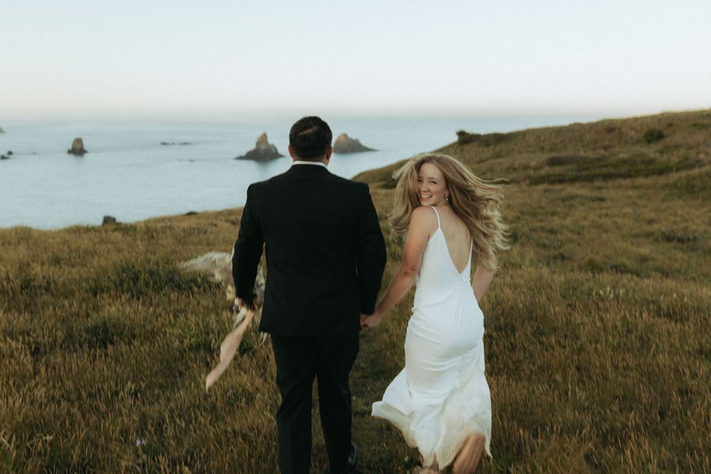 couple runs through field at Oregon Coast elopement wedding photoshoot