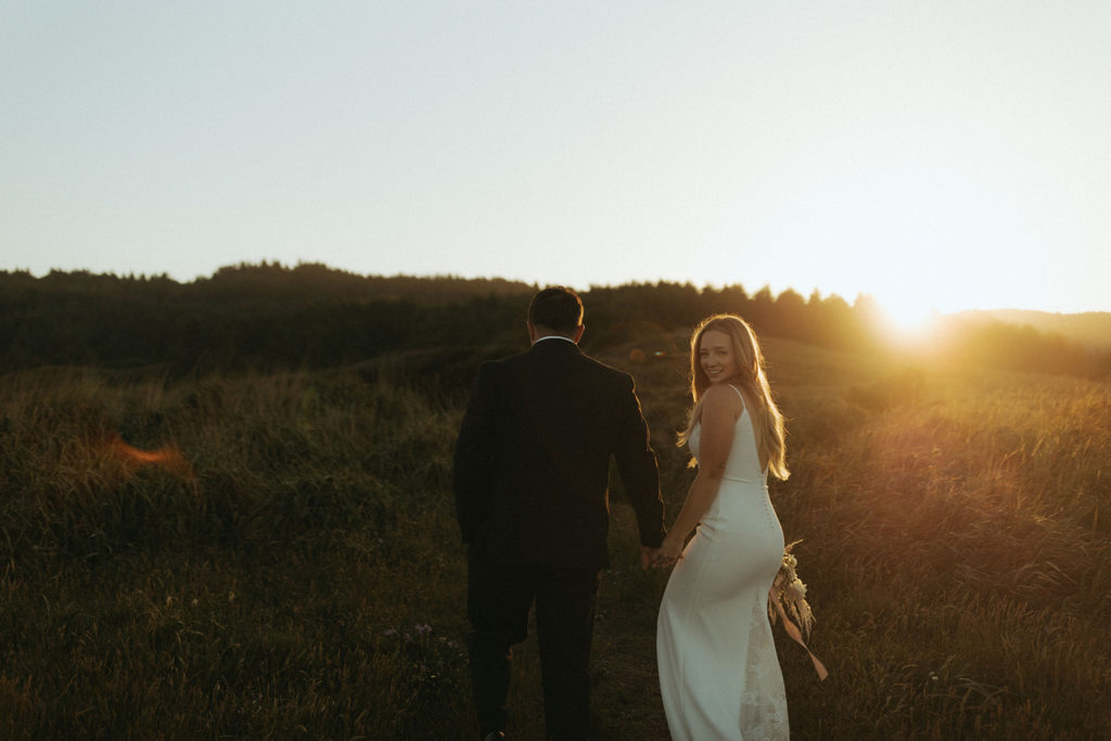couple walks through sunset field at Oregon Coast elopement 