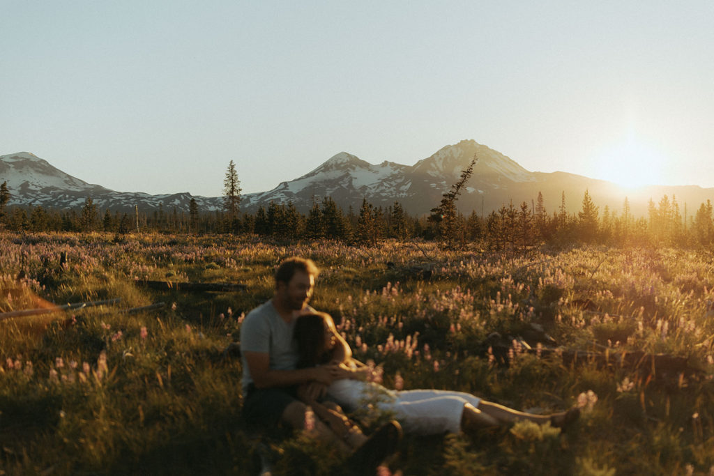 couple lies in field at mountainside engagement shoot