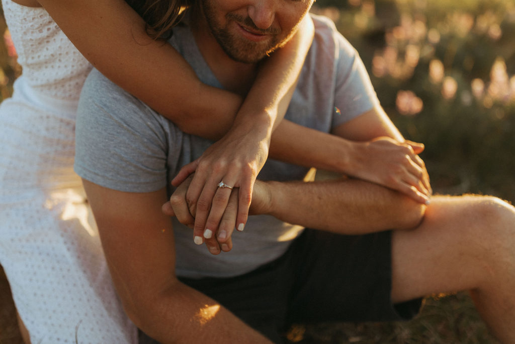 couple holds hands with engagement session in sunset field