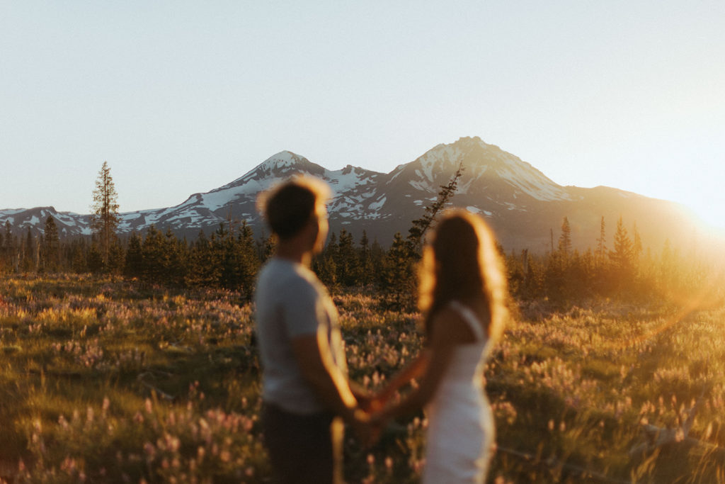 couple holds hands in sunset field at engagement session