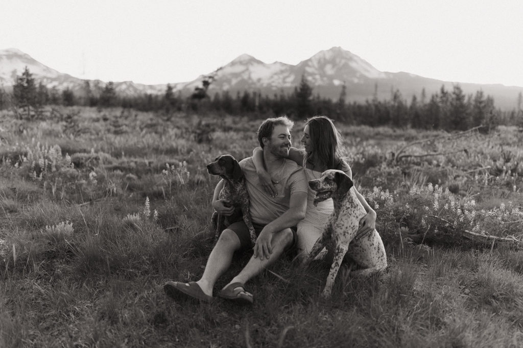 couple sits with dogs in field at Oregon engagement session