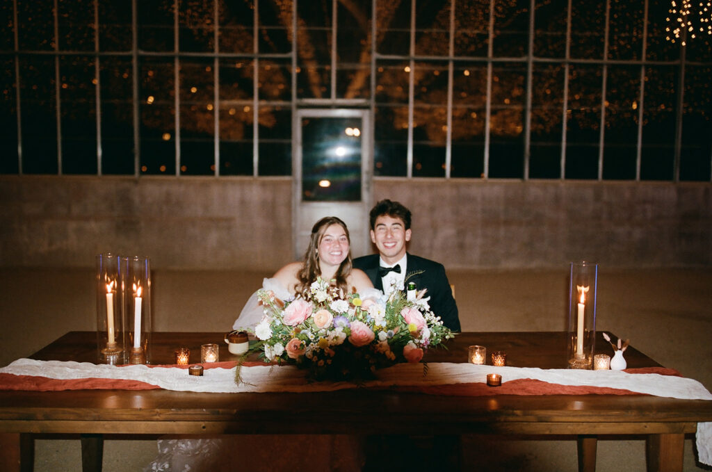 couple sits at head table as part of wedding film photography project

