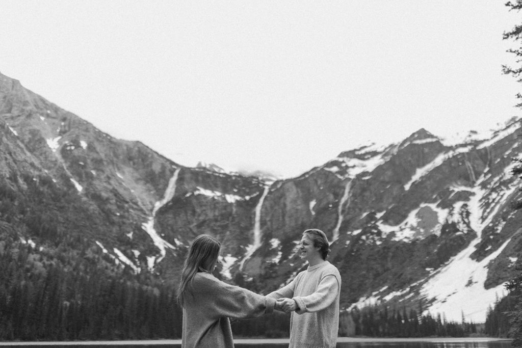 couple stands holding hands beside Avalanche Lake at Montana engagement