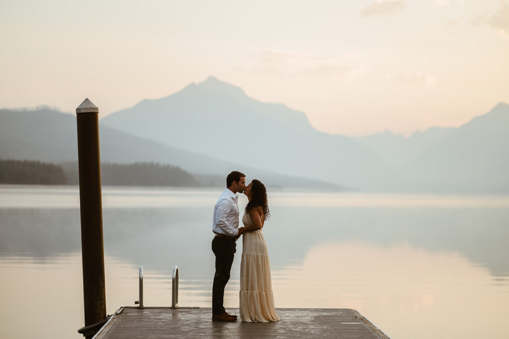 couple stands kissing on lake pier at sunset elopement