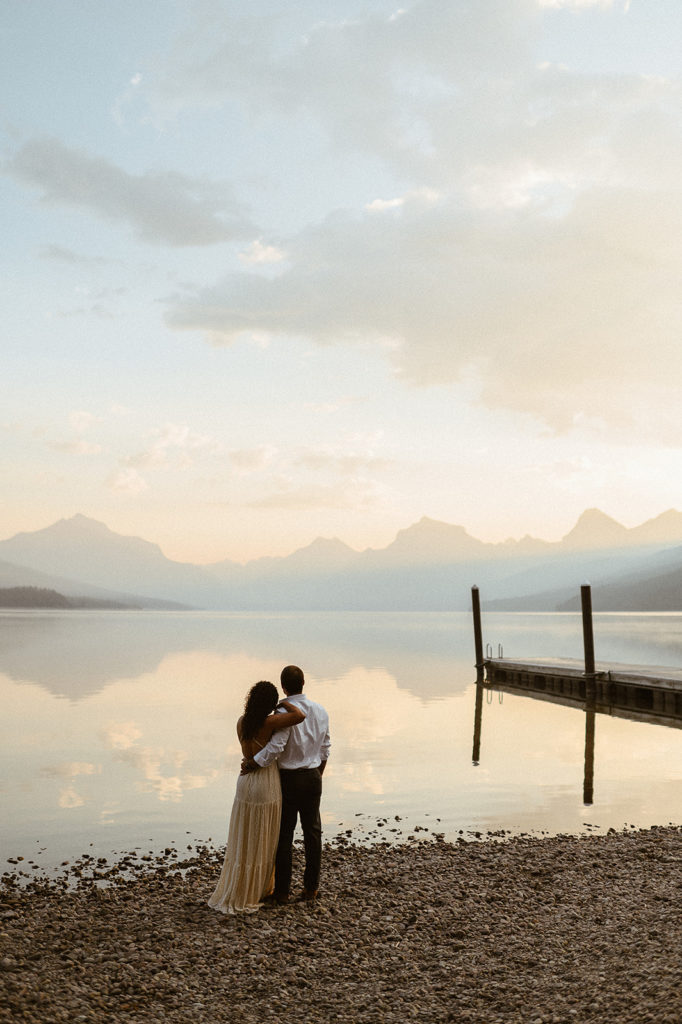 couple stands by lake at sunset engagement session
