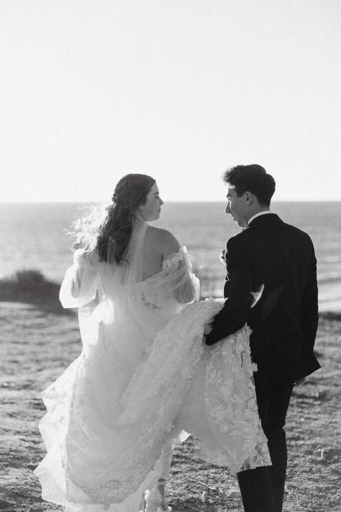 couple walks along water at California coast sunset wedding