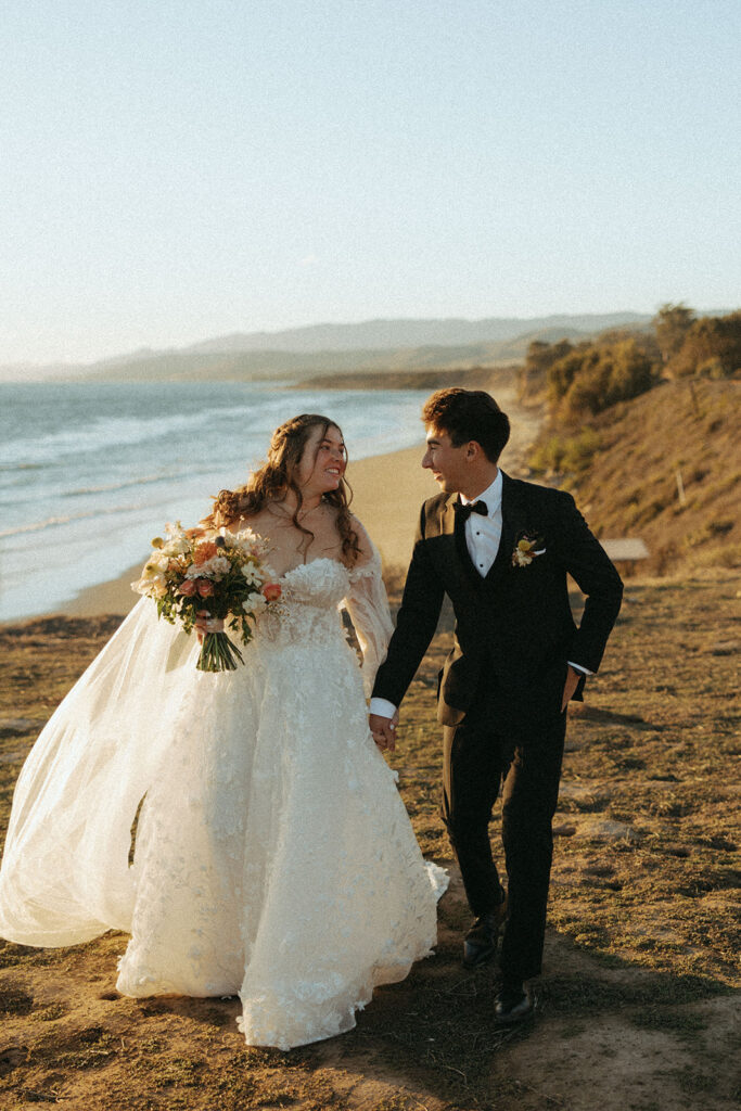 couple walks holding hands at California coast sunset wedding