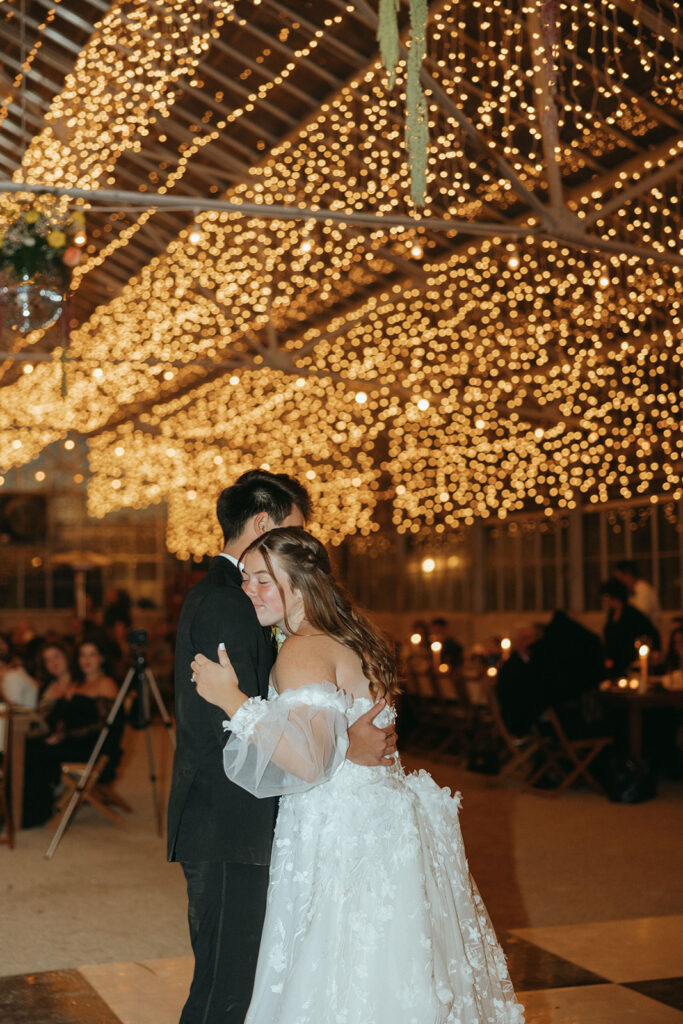 couple dances under twinkle lights at greenhouse wedding reception