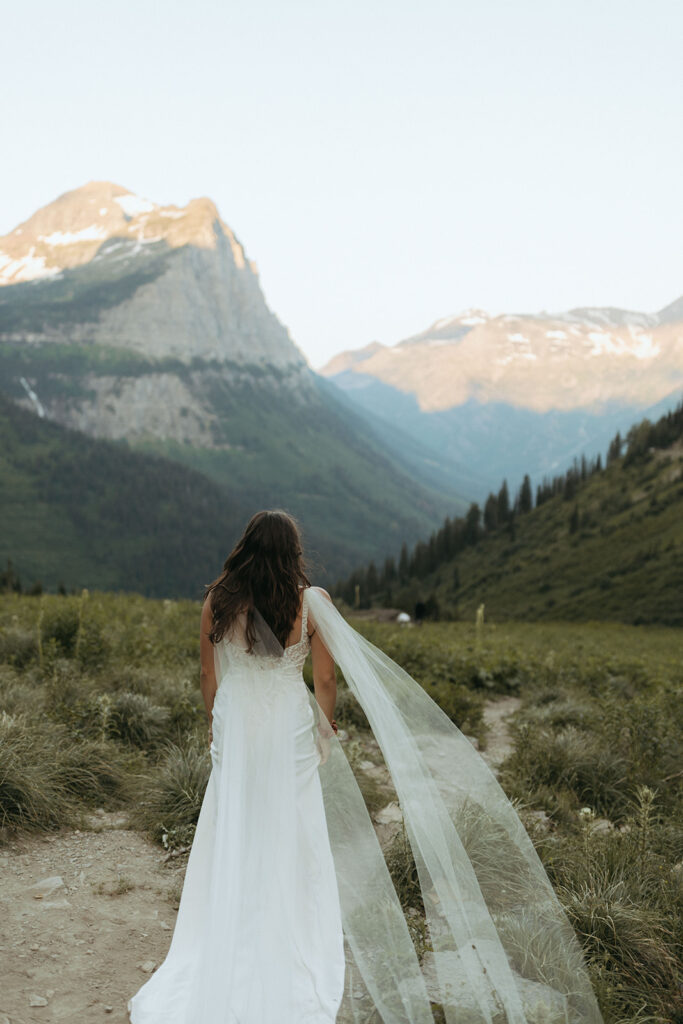 bride in wedding dress walking through grassy field beside mountain