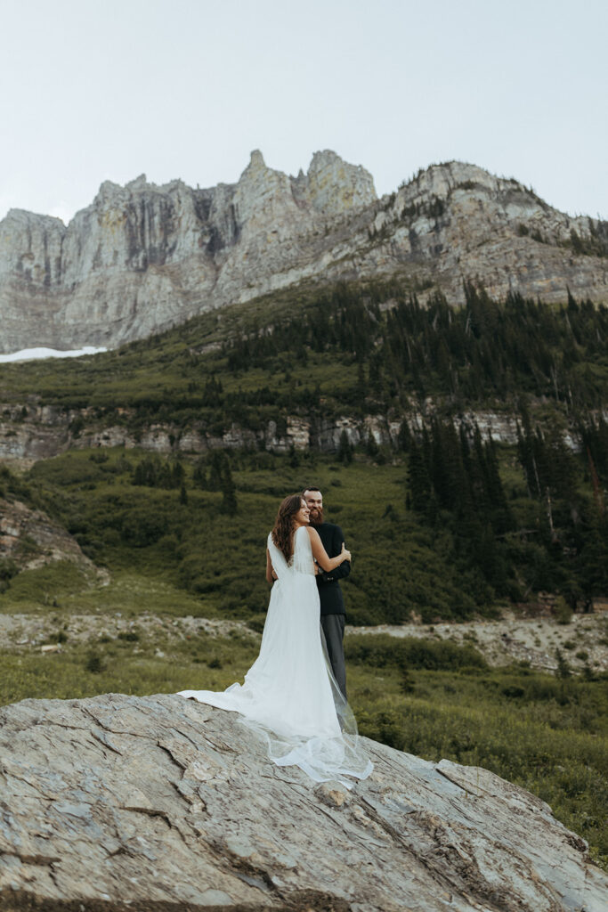 couple embraces standing on rock at Glacier National Park wedding