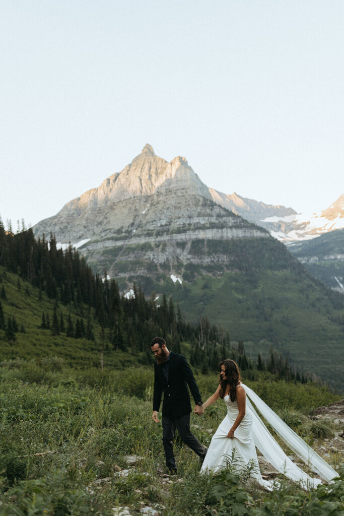 couple holds hands walking through field at Glacier National Park wedding