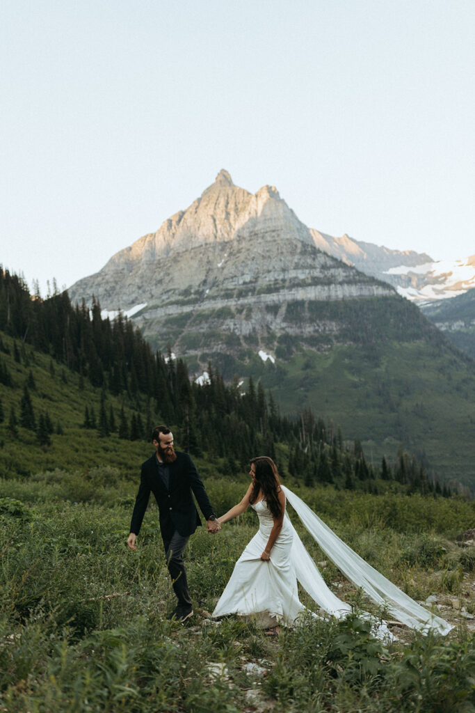 couple walks up hill holding hands at mountainside elopement