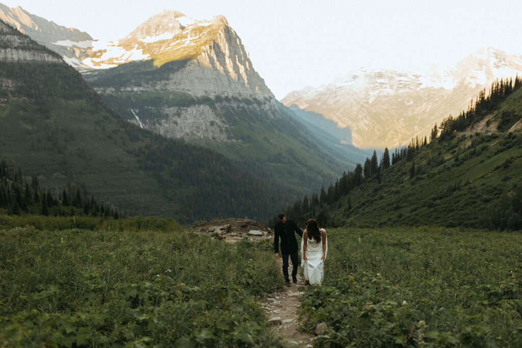 couple walks up hill at sunrise at Glacier National Park wedding