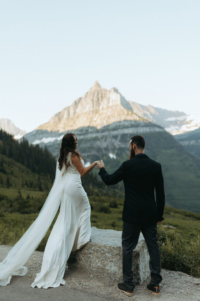 groom helps bride up on rock at outdoor elopement