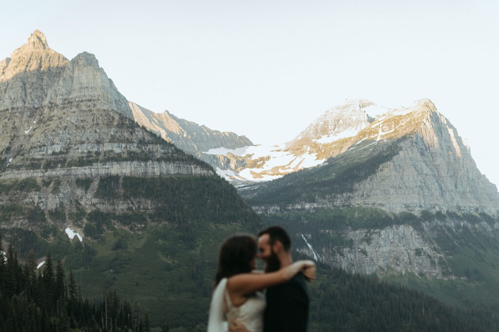 couple hugs standing in front of snow-covered mountains at Glacier National Park wedding