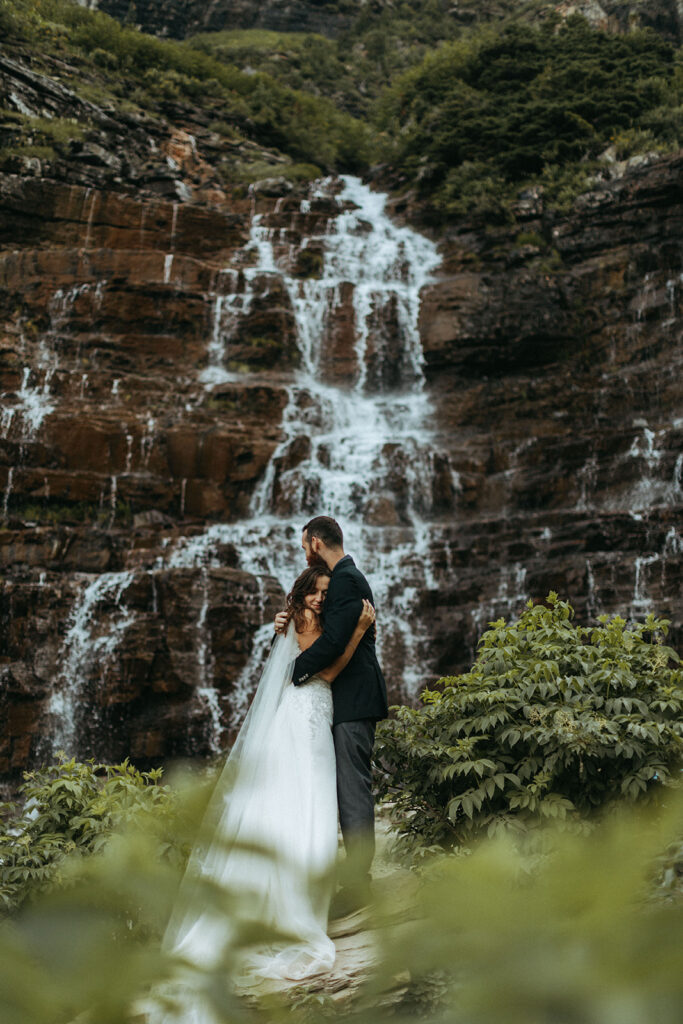 couple embraces beside waterfall at outdoor adventure elopement