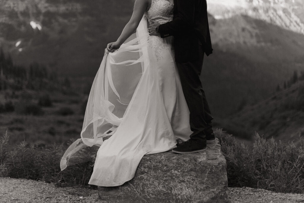 couple embraces standing on rock at Glacier National Park wedding